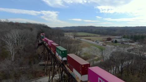 Aerial-Shot-Crossing-Over-a-Colorful-Intermodal-Train-on-the-Pope-Lick-Trestle-in-Louisville,-Kentucky-on-a-Sunny-Winter-Day