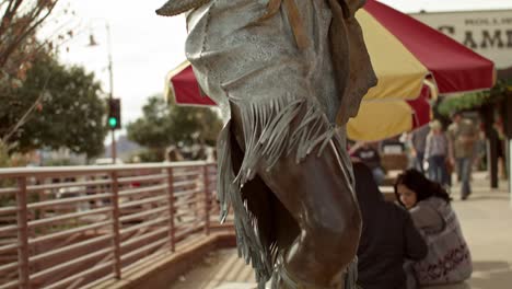 Native-American-woman-with-baby-in-papoose-sculpture-in-downtown-Sedona,-Arizona-with-people-in-the-background-and-video-tilting-down