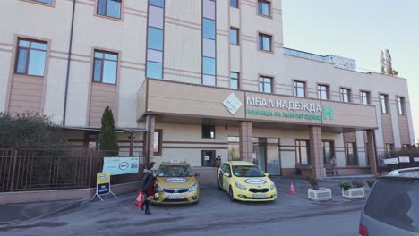 people-and-cars-in-front-of-the-main-entrance-of-Nadezhda-Women's-Health-Hospital-on-a-windy-winter-day
