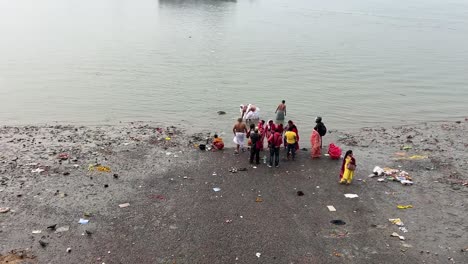 Wide-shot-of-people-bathing-and-offering-prayers-to-god-near-Hooghly-river-during-evening-in-Kolkata,-India