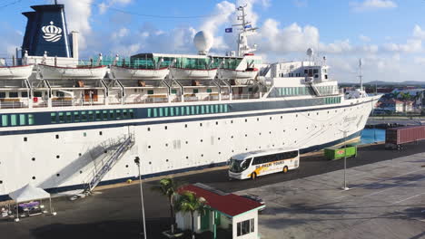 small-cruise-ship-rests-at-port-while-bus-awaits-nearby,-ready-to-embark-passengers-on-their-next-excursion-from-the-bustling-harbor