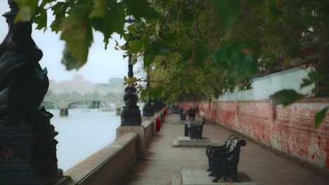 Benches-on-the-walkway-along-the-River-Thames-in-London,-distant-blurry-people