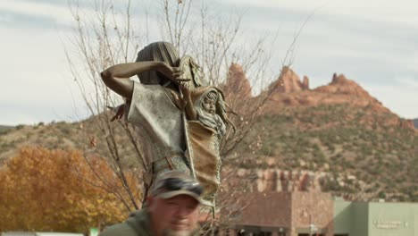 Native-American-woman-with-baby-in-papoose-sculpture-in-downtown-Sedona,-Arizona-with-people-walking-by