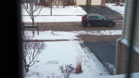 Departing-car-on-road-with-snow-seen-from-house-window-high-angle-slow-motion