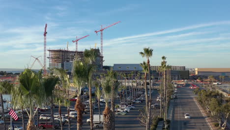 The-new-convention-center-being-build-in-Chula-Vista-California,-drone-rising-from-behind-palm-trees