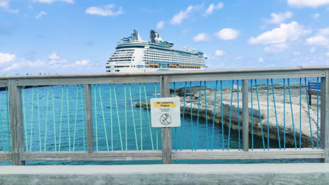 Amidst-the-grandeur-of-docked-cruise-ship,-whimsical-caution-sign-on-the-bridge-adds-touch-of-humor-to-the-bustling-waterfront-scene-|-funny-caution-sign-on-island-with-cruise-ship-docked