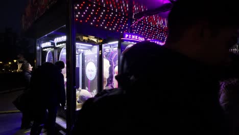 Nachtaufnahmen-Von-Menschen-An-Pink-Date-Arcade-Spielautomaten,-An-Denen-Man-Das-Seil-Durchtrennen-Muss,-Das-Einen-Riesigen-Teddybären-Hält,-Um-Es-Zu-Gewinnen