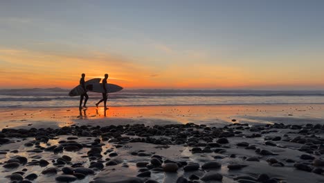 Silhouetten-Von-Surfern,-Die-Während-Eines-Wunderschönen-Sonnenuntergangs-Am-Strand-Spazierten