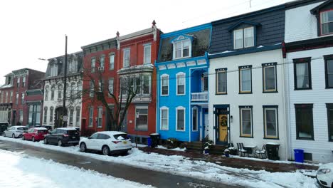 Row-of-colorful-townhouses-with-snow-on-the-sidewalk-and-parked-cars