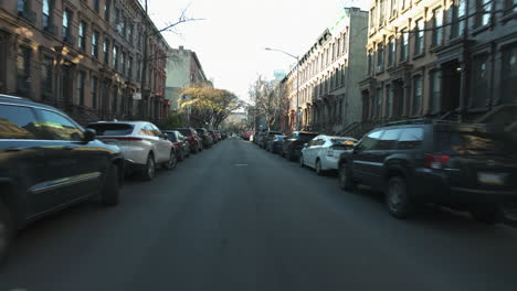 Driving-in-middle-of-traditional-rowhouses,-sunny,-autumn-day-in-New-York