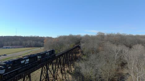 Aerial-Shot-Following-Two-Norfolk-Southern-Engines-Leading-a-Mixed-Freight-Train-across-the-Pope-Lick-Trestle-in-Louisville,-Kentucky-on-a-Sunny-Winter-Day