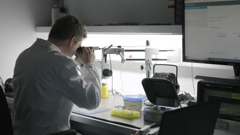 Wide-shot-of-Male-Scientist-in-lab-looking-at-sample-using-microscope