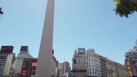 Tiro-Revelador,-Obelisco-De-Buenos-Aires-En-La-Avenida-9-De-Julio,-Brillando-Sobre-El-Horizonte-Soleado,-Obelisco,-Autos-Pasando