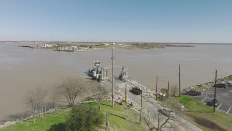 An-aerial-establishing-shot-of-the-Lynchburg-Ferry-docking,-with-cars-unloading-at-the-San-Jacinto-Battlefield-Site-along-the-Houston-Ship-Channel-in-La-Porte,-Texas