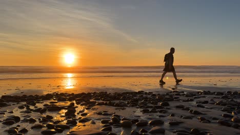 Hiker-silhouetted-walking-on-beach-during-a-beautiful-sunset