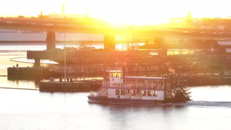 Paddle-steamer-boat-on-river-at-sunrise-with-naval-ship-and-industrial-backdrop