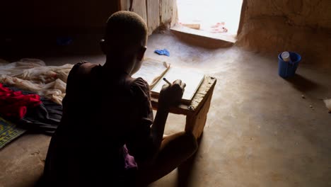 Rückansicht-Eines-Jungen-Afrikanischen-Jungen,-Der-Tagsüber-Im-Dorf-Wulugu,-Ghana,-Auf-Ein-Notizbuch-Schreibt