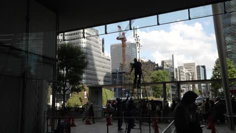 Silhouette-View-Of-Tokyo-Station-Maintenance-Workers-Cleaning-Windows-At-Yaesu-Entrance-side-With-Commuters-Walking-Past