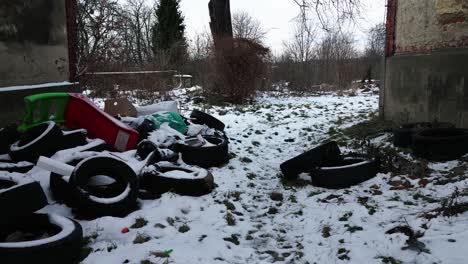 An-abandoned,-snowy-outdoor-space-between-houses-littered-with-discarded-tires-and-trash