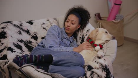 Woman-lying-on-a-rocking-chair-caresses-her-dog-and-talks,-puppy-with-cute-scarf-relaxing-with-owner,-gentle-pure-breed,-Labrador-Retriever-chilling-at-home,-dog-mom,-pet-parenting,-daycare,-pure-love