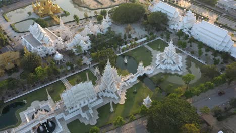 Aerial-drone-of-Wat-Rong-Khun-the-amazing-buddhist-White-Temple-and-Golden-Temple-with-mountains-and-landscape-in-Chiang-Rai,-Thailand