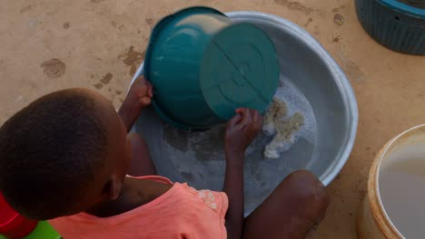 Kleines-Schwarzes,-Süßes-Afrikanisches-Kind,-Das-Geschirr-In-Einem-Plastikwassertank-In-Einem-Abgelegenen-Ländlichen-Dorf-Wäscht