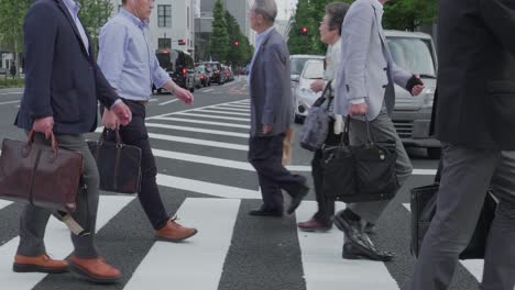 Varios-Empresarios-Japoneses-Cruzando-Una-Calle-En-El-Centro-De-Tokio,-Japón,-En-Un-Día-Nublado