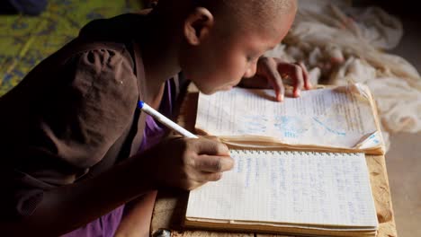 Nahaufnahme-Eines-Ländlichen-Afrikanischen-Jungen,-Der-Im-Dorf-Wulugu-In-Ghana-Notizen-Auf-Sein-Notizbuch-Schreibt