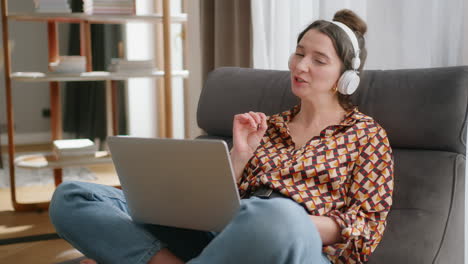 Smiling-European-woman-wearing-headphones-with-laptop-on-lap-has-video-call