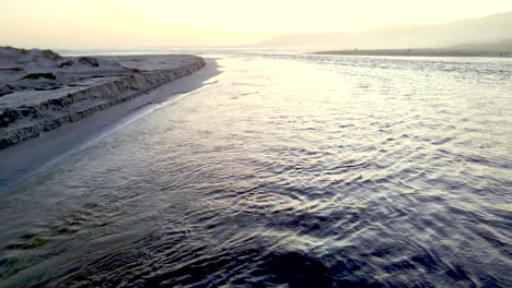 Lagoon-mouth-breaching-sandbar-to-divulge-into-ocean-at-sunset