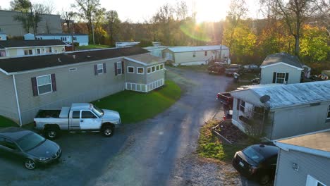 Sunlit-mobile-home-park-with-vehicles-and-surrounding-autumn-trees