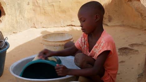 Niedliche-Kleine-Schwarzafrikanische-Kinder,-Die-In-Einem-Abgelegenen-Ländlichen-Dorf-Geschirr-Auf-Einem-Eimer-Spülen