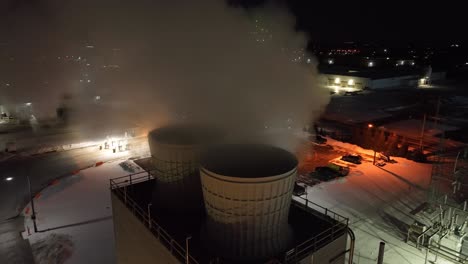 Industrial-site-with-steam-towers-emitting-vapor-against-a-dark-sky-at-night