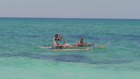 two-young-men-paddling-in-a-small-boat-over-the-pacific-ocean-in-the-philippines