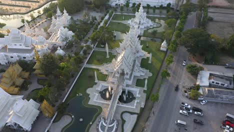 Aerial-drone-of-Wat-Rong-Khun-giant-buddhist-White-Temple-and-Golden-Temple-with-mountains-and-landscape-in-Chiang-Rai,-Thailand