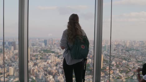 a-western-tourist-standing-in-front-of-the-Tokyo-Skyline-while-sunset-enjoying-the-view