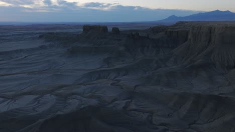 Aerial-flyover-man-standing-on-ridge-overlooking-eerie-Factory-Butte-moonscape-at-dawn