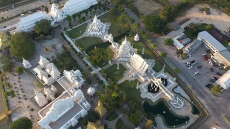 Aerial-drone-of-Wat-Rong-Khun-stunning-buddhist-White-Temple-and-Golden-Temple-with-mountains-and-landscape-in-Chiang-Rai,-Thailand