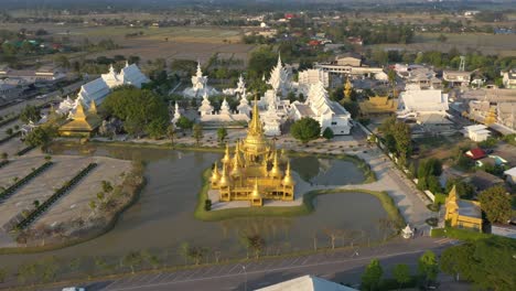 Aerial-drone-flying-backwards-of-Wat-Rong-Khun-the-giant-buddhist-White-Temple-and-Golden-Temple-with-mountains-and-landscape-in-Chiang-Rai,-Thailand