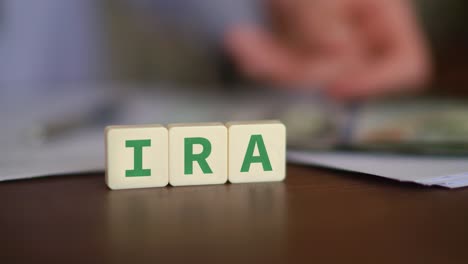 Buchstabenblöcke,-Die-IRA-Bilden,-Mit-Einer-Person,-Die-Geld-Zählt,-Vor-Unscharfem-Hintergrund