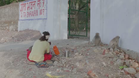 Homeless-Person-Sitting-On-The-Ground-In-The-Dirt-Next-To-Rubbish-And-Monkeys