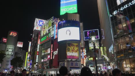 Handheld-Zeitlupenaufnahme-Von-Werbetafeln-Und-Menschen,-Die-Nachts-Am-Shibuya-Kreuz-Spazieren