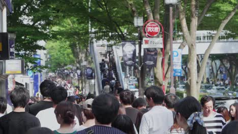 Handheld-slow-motion-rear-view-of-pedestrians-walking-by-lush-green-trees-in-Tokyo