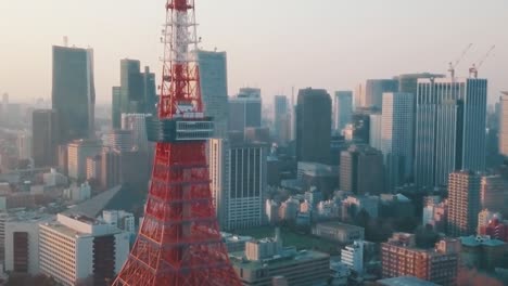 Drone-aerial-above-Tokyo-City-panning-around-the-iconic-red-Tokyo-Tower-surrounded-by-tall-skyscrapers-during-a-stunning-sunset-with-blue-and-orange-skies