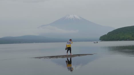 Handheld-shot-of-young-male-on-sandbank-in-calm-lake-front-of-Mount-Fuji-Tokyo