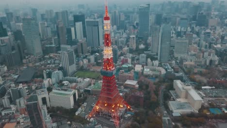 Luftaufnahme-über-Der-Stadt-Tokio,-Schwenk-Um-Den-Ikonischen-Roten-Tokio-Turm,-Umgeben-Von-Hohen-Wolkenkratzern,-Während-Eines-Atemberaubenden-Sonnenuntergangs-Mit-Blauem-Und-Orangefarbenem-Himmel