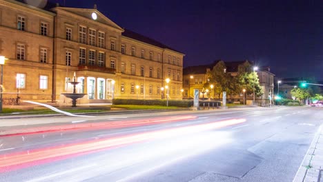 Ein-Wunderschöner-Zeitraffer-Des-Historischen-Gebäudes-Der-Universität-Tübingen-Bei-Nacht-Mit-Einem-Springbrunnen-Und-Vorwärtsfahrenden-Autos