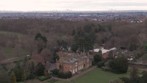 Aerial-drone-shot-of-Addington-Palace-in-Croydon,-London,-United-Kingdom-on-a-cloudy-day-and-with-London-Downtown-Cityscape-in-the-background