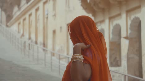 Indian-woman-hiding-herself-under-an-orange-scarf-in-Jodhpur,-India