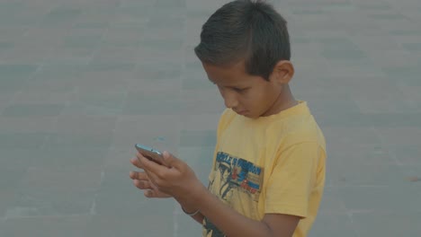 Junger-Indischer-Junge-Allein-Auf-Der-Straße,-Der-Auf-Einem-Mobiltelefon-Spielt